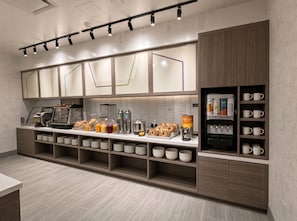 Um balcão de café da manhã moderno, com máquina de café, estação de waffles e diversos pães e doces.