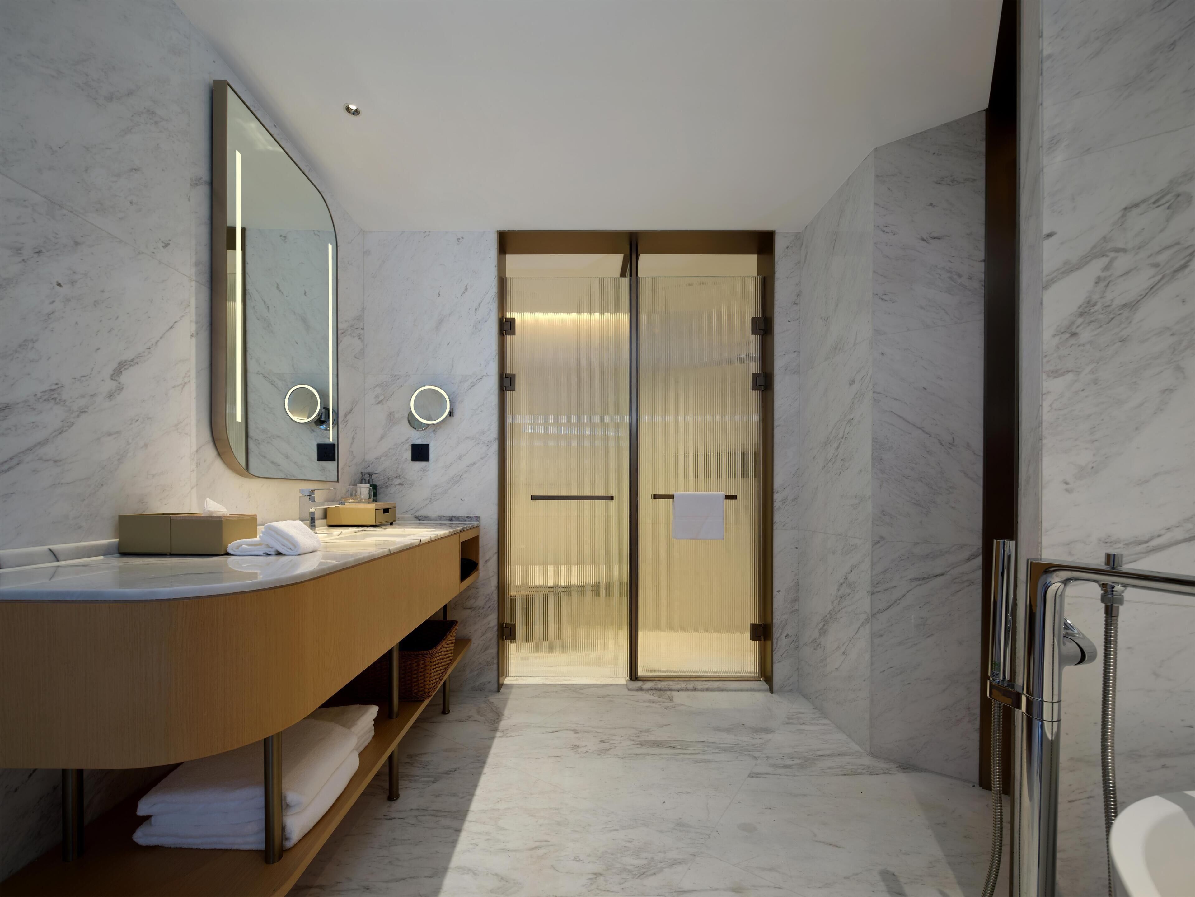 A modern bathroom with a marble floor, a wooden vanity, a large mirror, and a shower area.