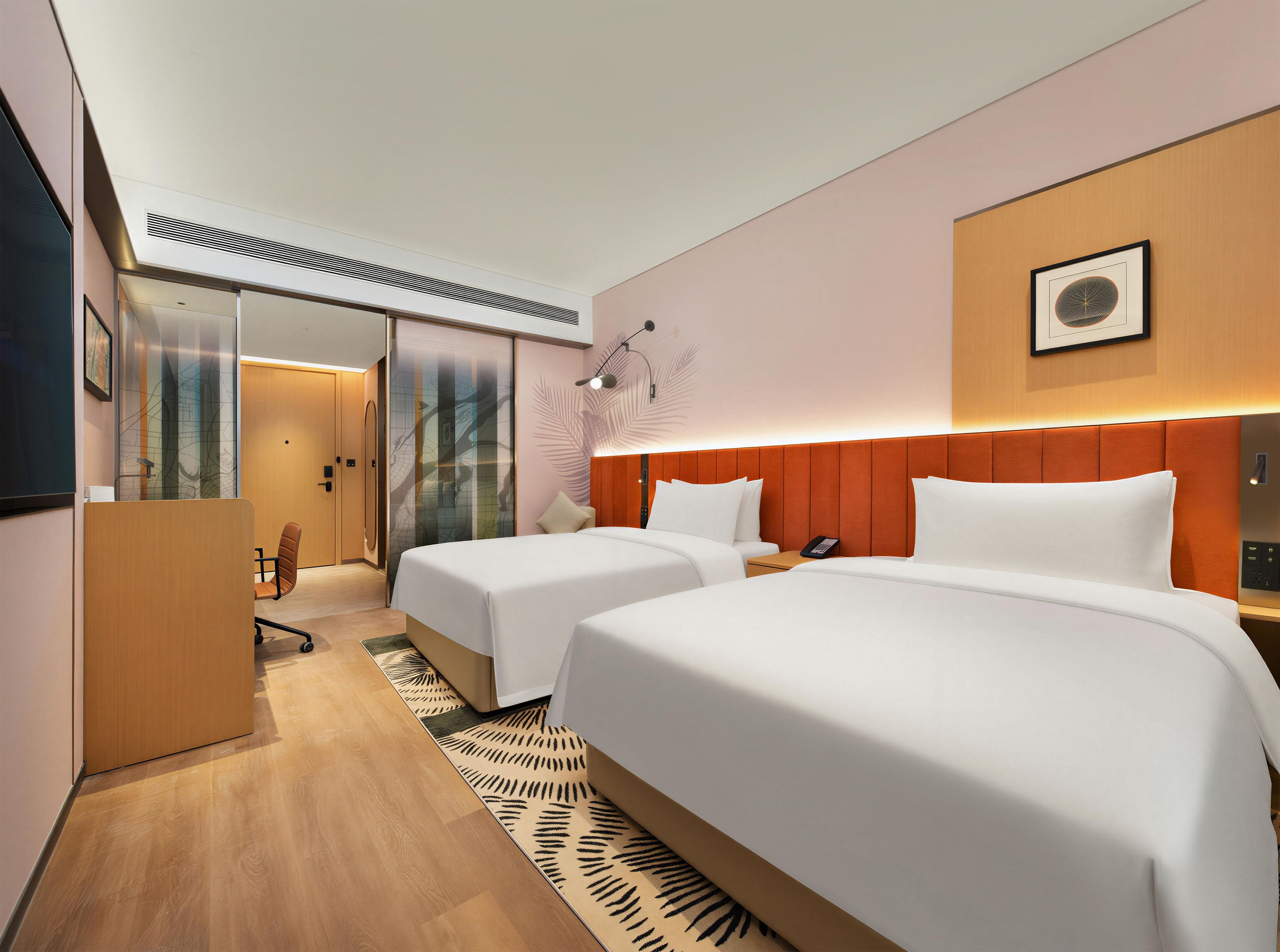 A hotel room with two beds, a desk, a chair, a desk lamp, a wall-mounted phone, and a picture frame.