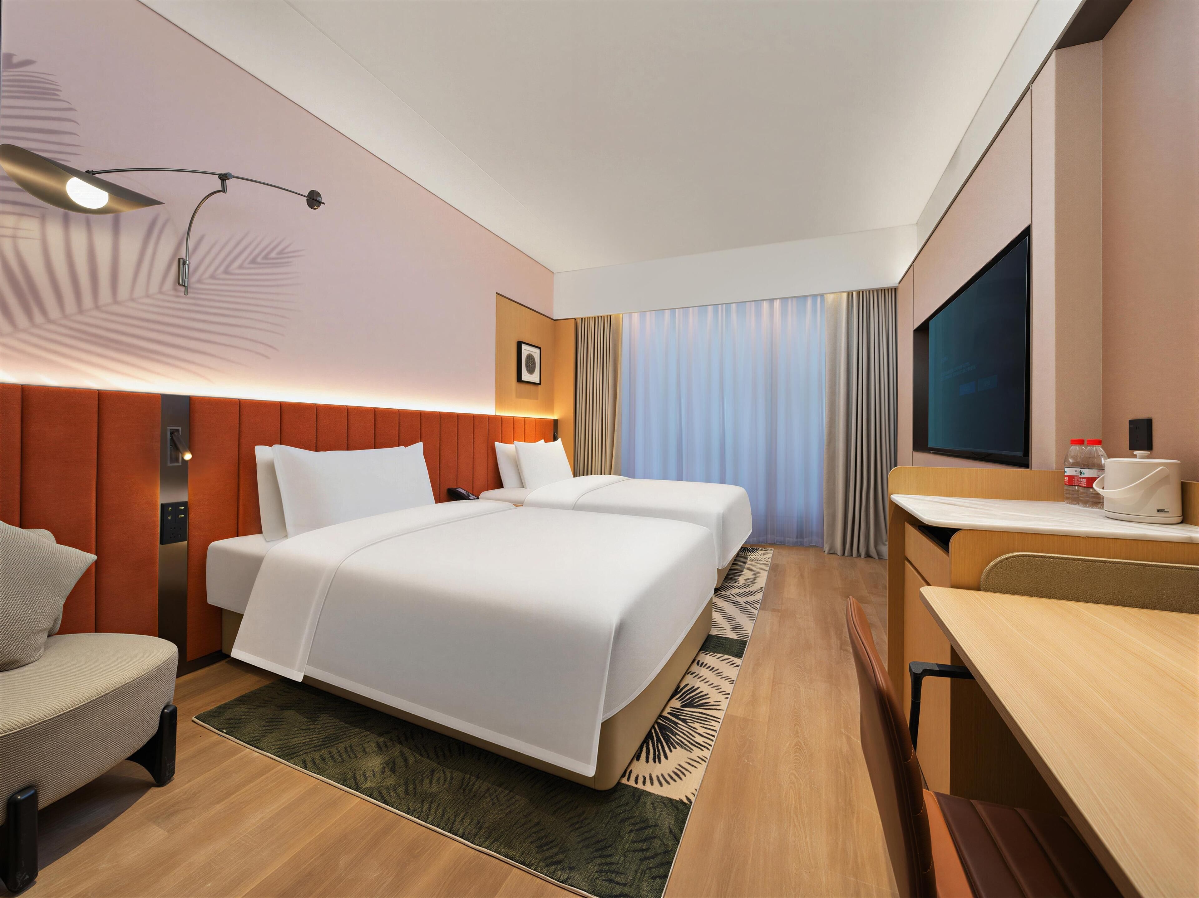 A hotel room with two beds, a desk, a chair, a TV, and a minibar.