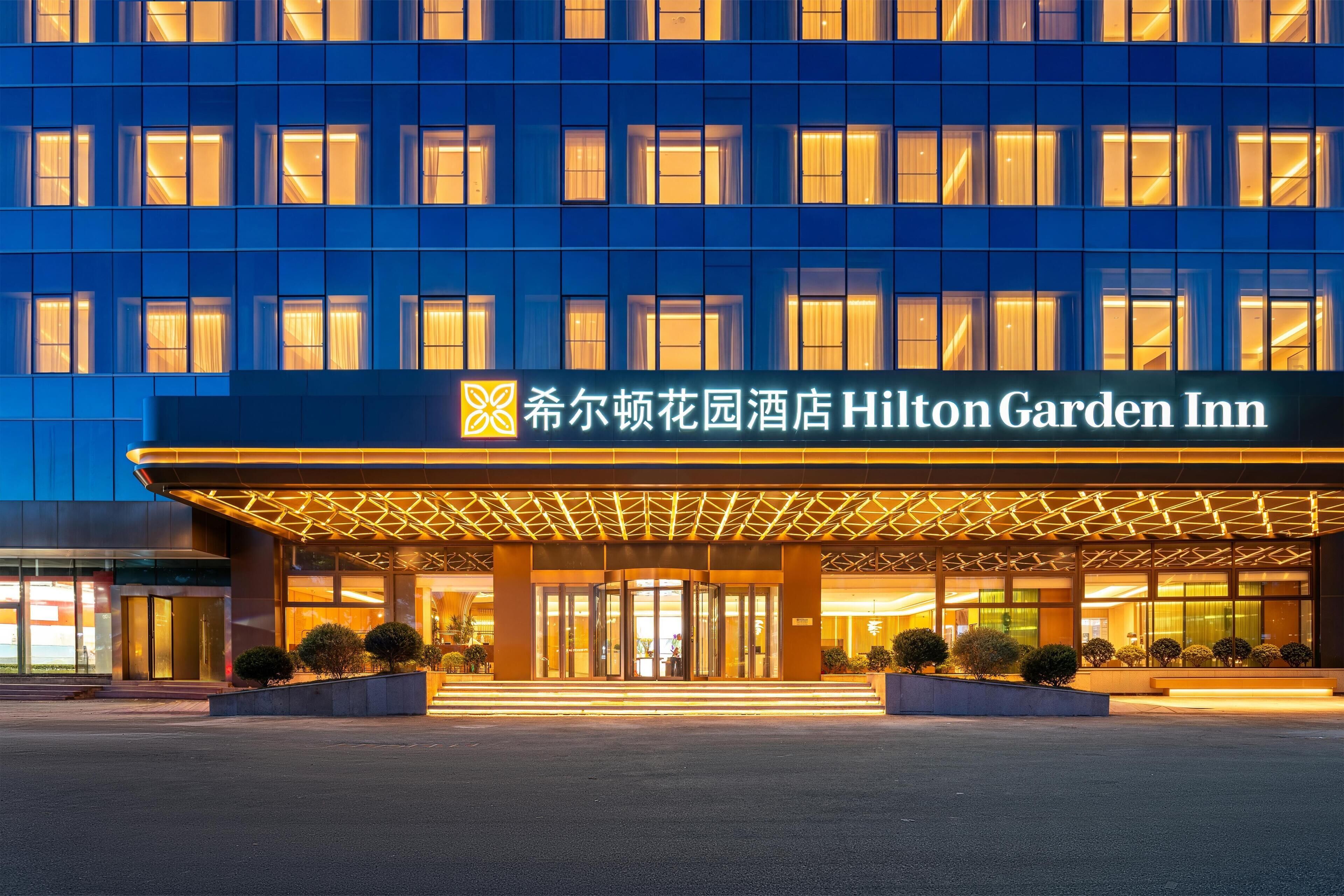 A hotel entrance with a modern facade, illuminated signage, and a well-lit entrance area.