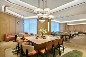 Una sala conferenze di un hotel moderno con tavoli rotondi, sedie e un'elegante composizione floreale al centro.