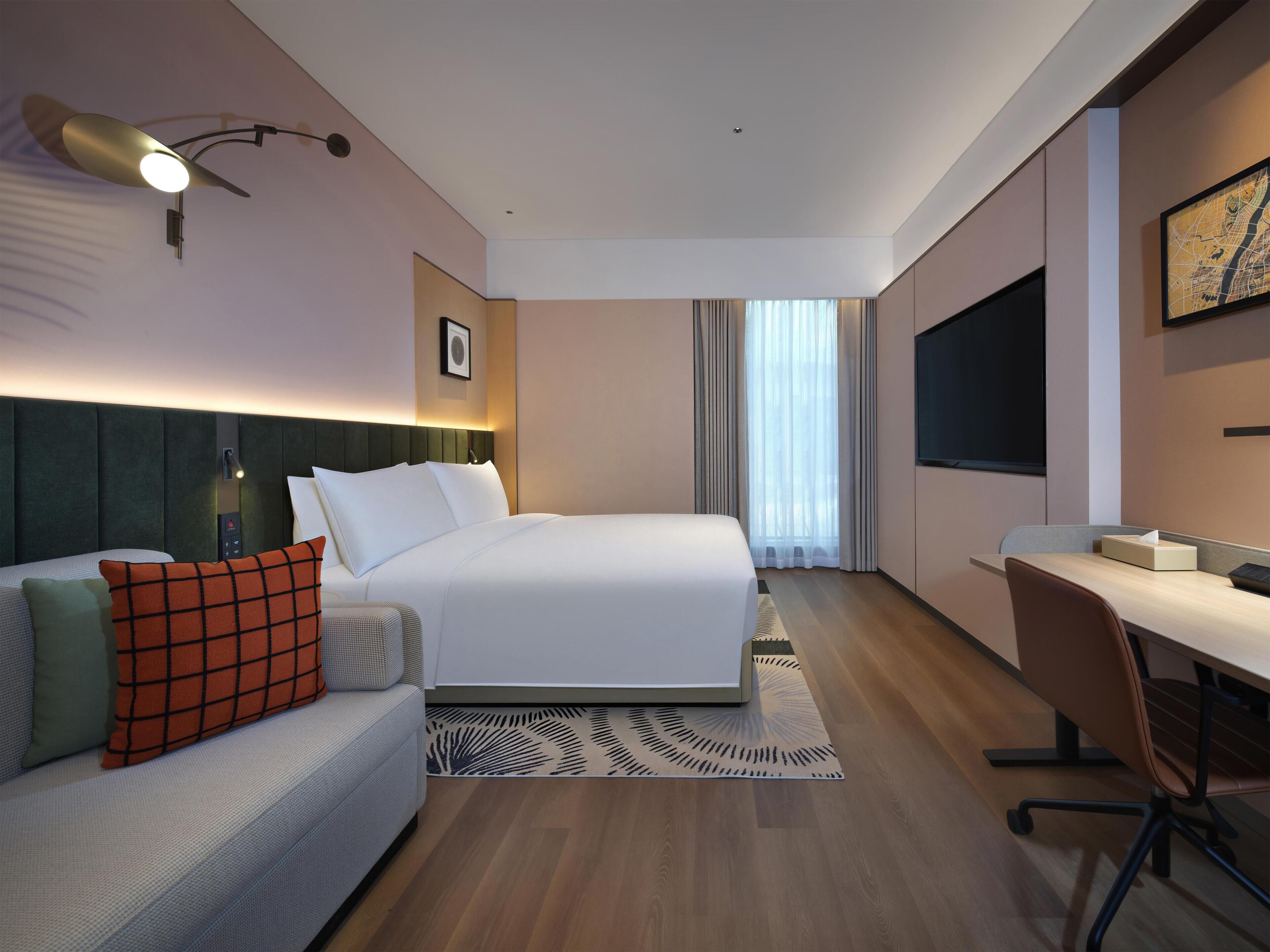 A hotel room with a bed, a desk, a chair, a sofa, and a TV.