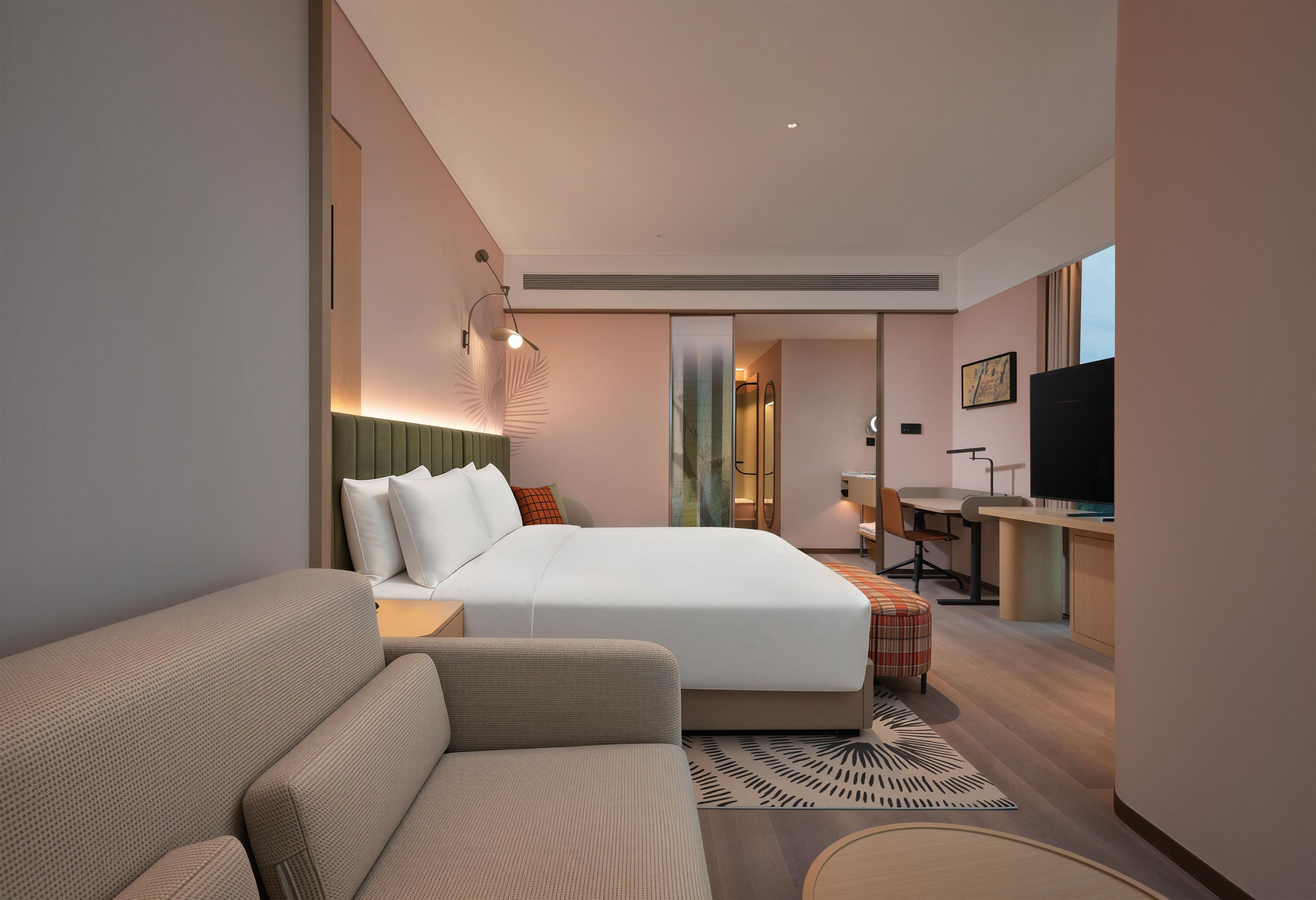 Ett modernt hotellrum med en stor säng, en soffa, ett skrivbord och en tv.