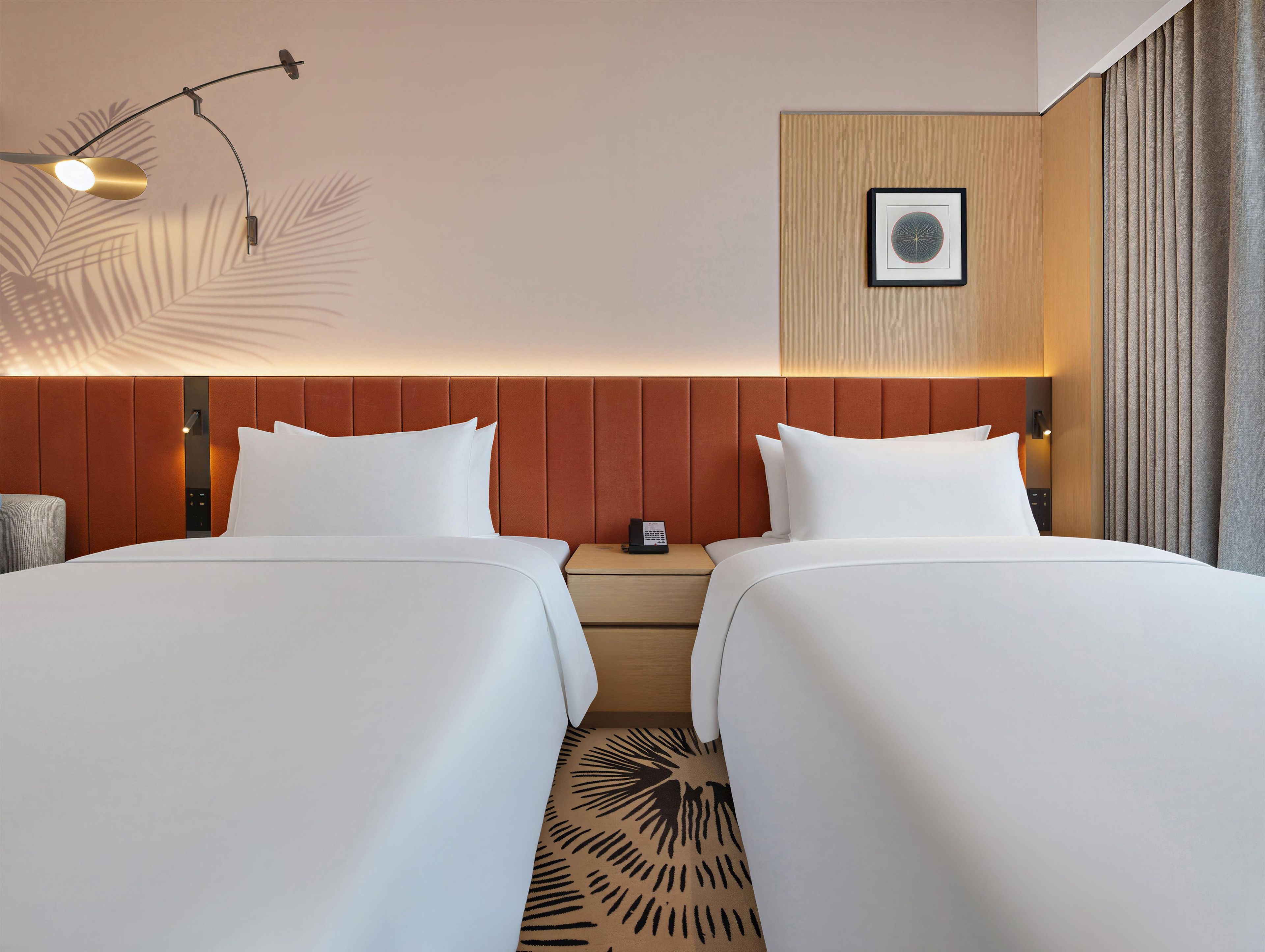 A hotel room with two beds, a nightstand, a wall-mounted picture, and a ceiling light fixture.