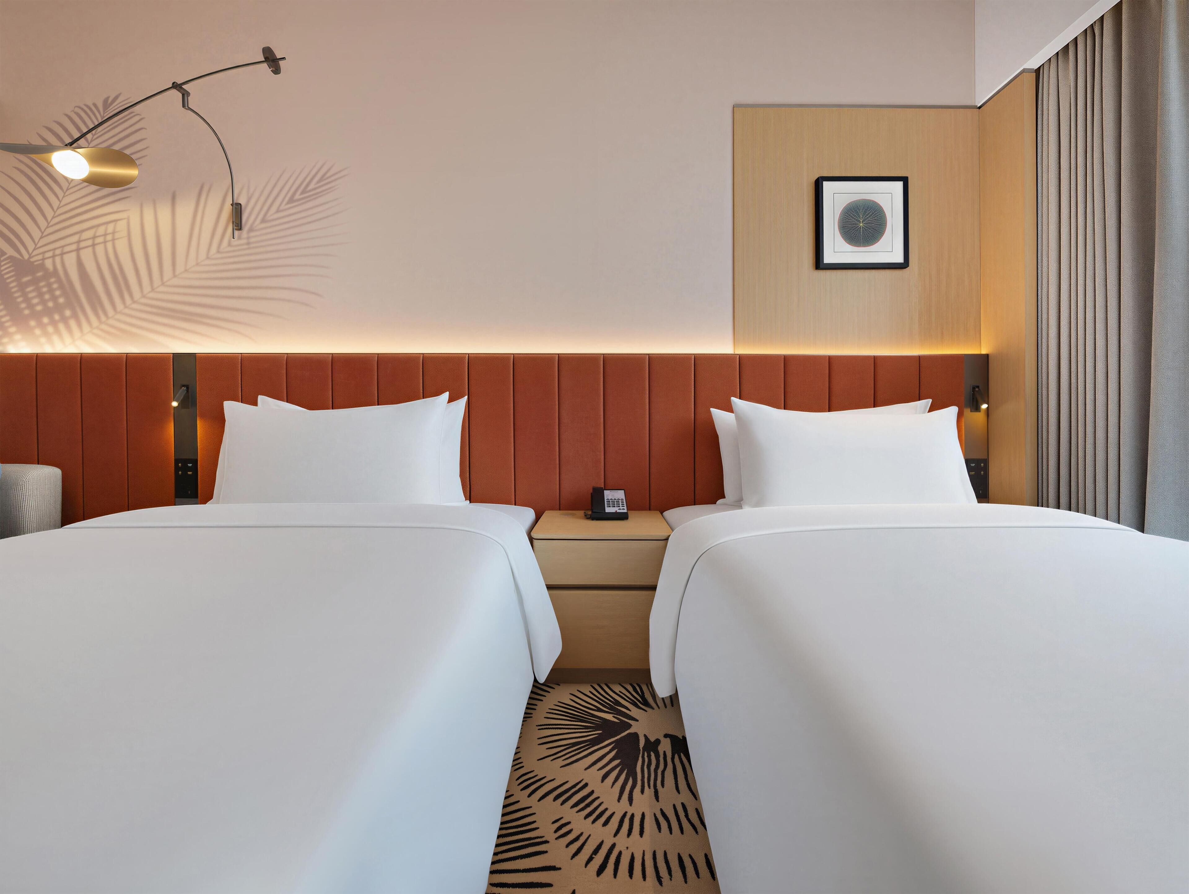 Habitación de hotel con dos camas, una mesita de noche, un cuadro en la pared y una lámpara del techo.