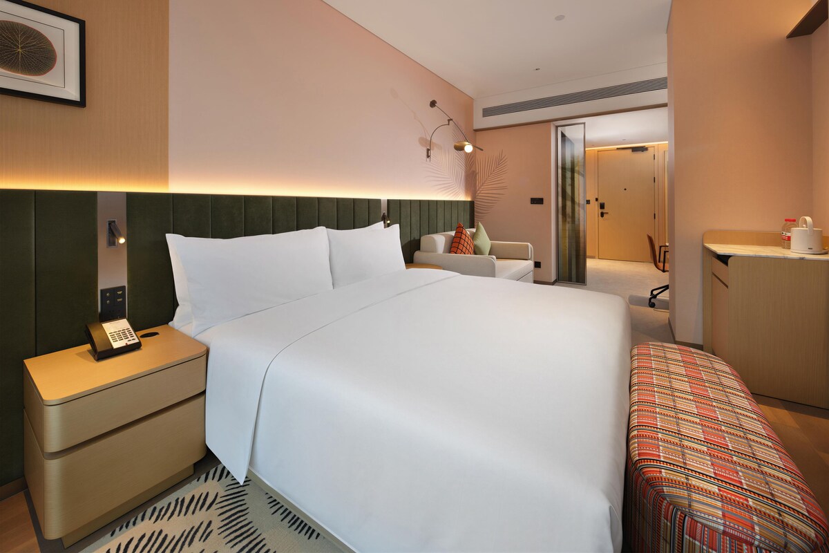 Une chambre d’hôtel comprenant un lit, une table de chevet, une lampe et un petit coin salon avec une chaise et une table.