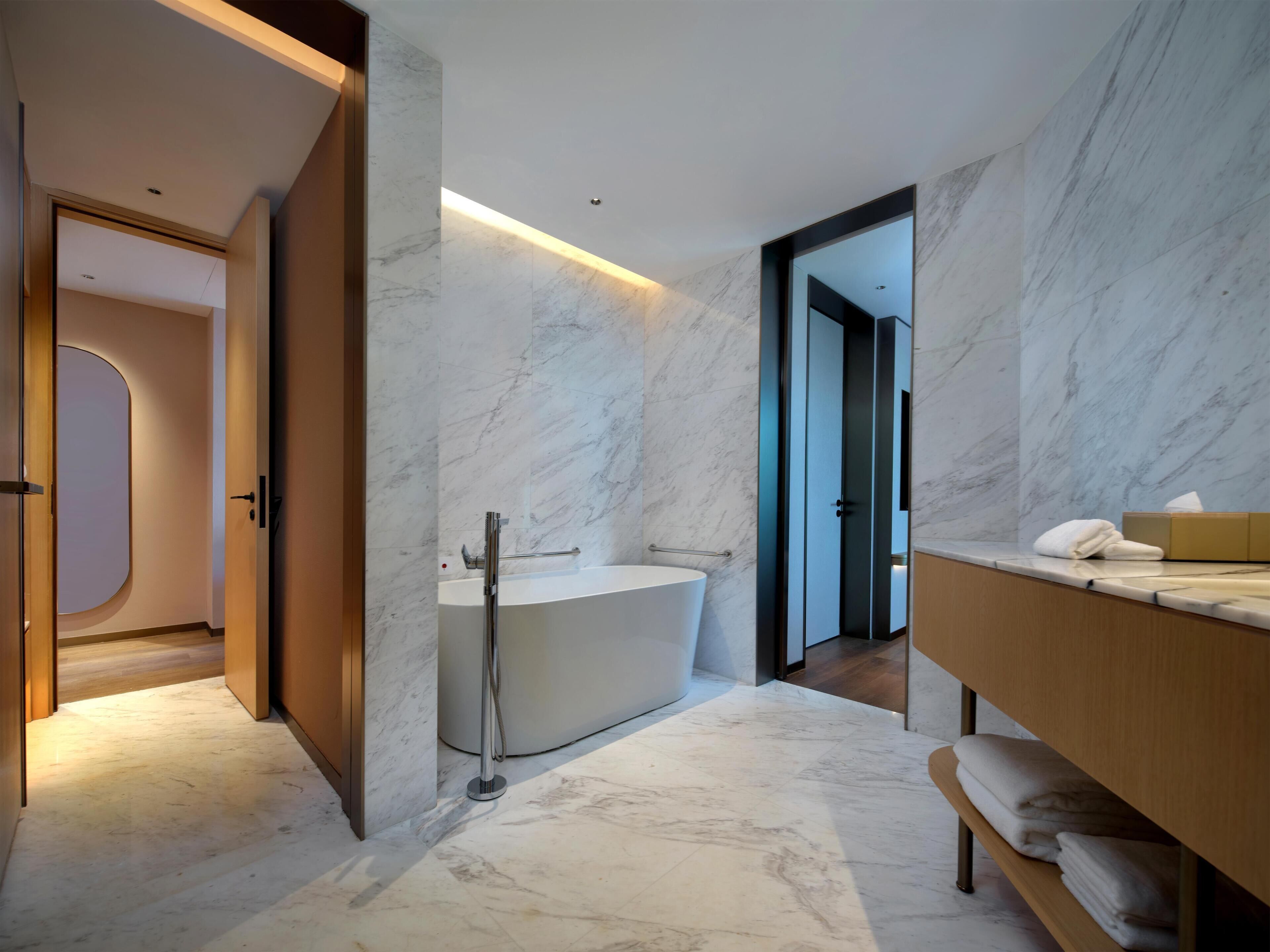 Un baño moderno con una bañera independiente, un tocador de madera y paredes de mármol.