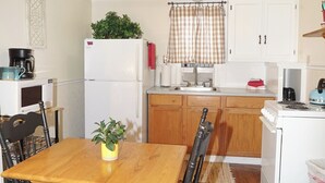 Una cocina compacta con electrodomésticos blancos, una mesa de comedor de madera y una ventana pequeña con cortinas.