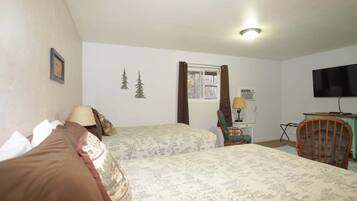 A bedroom with two beds, a television, and a desk with a lamp.
