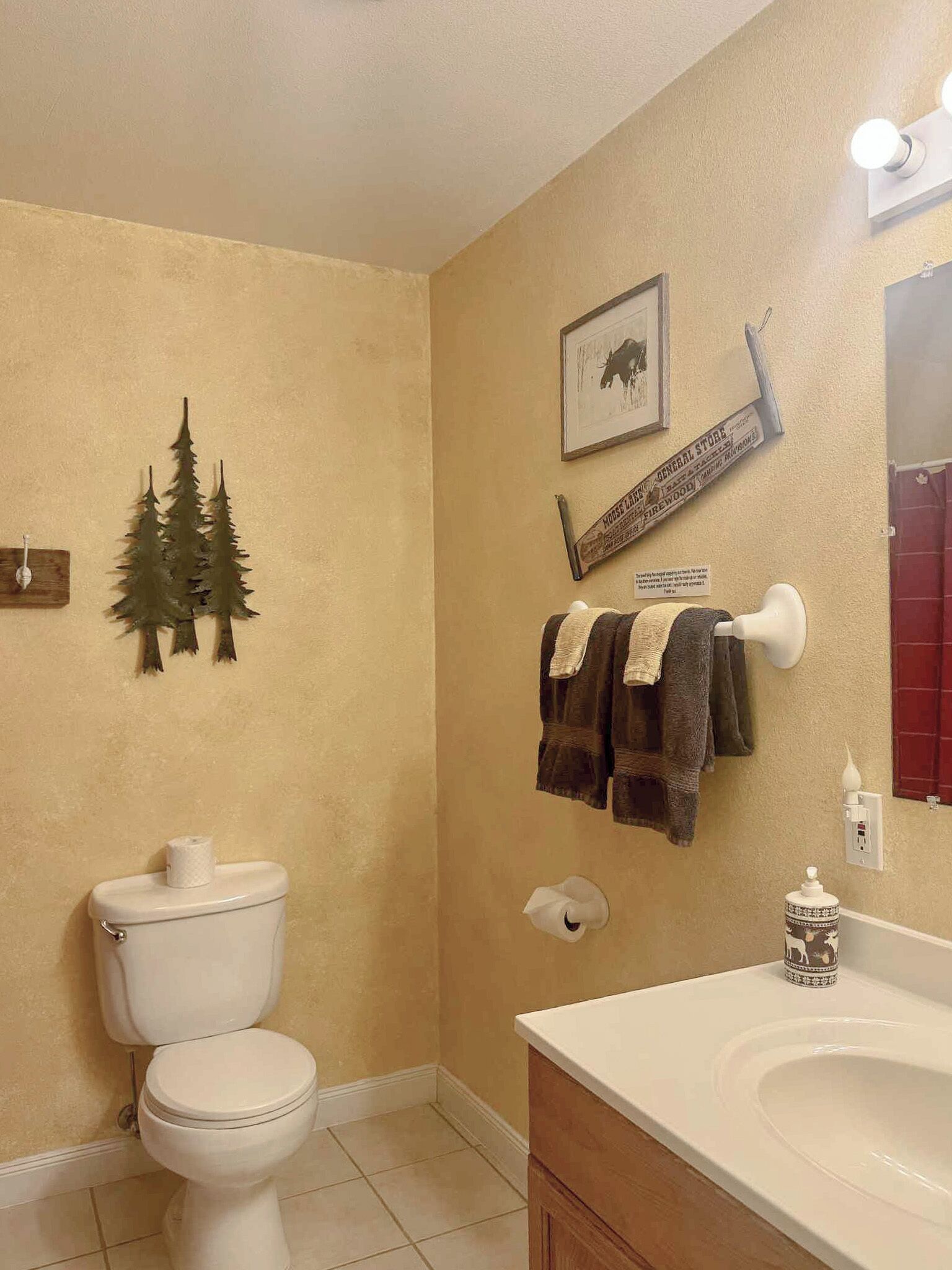 Un baño con inodoro, lavamanos y detalles decorativos como un cuadro enmarcado y un perchero.