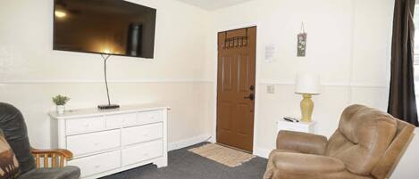 Een woonkamer met een televisie, een bruine leren fauteuil, een witte dressoir en een houten salontafel.