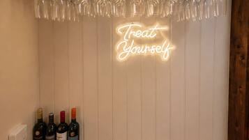 A bar area with a neon sign reading 'Treat Yourself,' wine bottles, and a welcome mat for The Scullery Bar.
