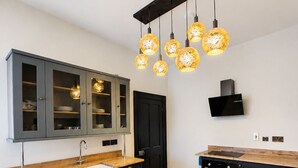 Une cuisine moderne dotée d’un îlot central, de meubles de rangement noirs, d’un four encastré et d’un luminaire suspendu original.