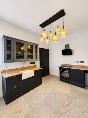 A modern kitchen with a central island, black cabinetry, a built-in oven, and a unique hanging light fixture. - No.60 Sligo (Sligo)
