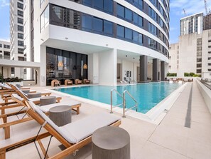 Ein modernes Hotel mit Swimmingpool, Liegestühlen und einer großen Glasfassade.