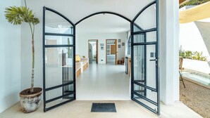 Un intérieur moderne avec une entrée dotée d’une porte en verre, une plante en pot et une vue sur un espace de vie comprenant un canapé et une table à manger.