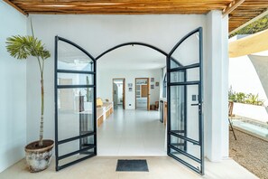 Ein modernes Interieur mit Glastür, einem Blumentopf und Blick in einen Wohnbereich mit Sofa und Esstisch.