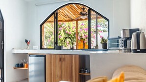 Une cuisine compacte dotée d’un lave-vaisselle intégré, de meubles en bois et d’une grande fenêtre donnant sur un jardin où poussent des fleurs roses.