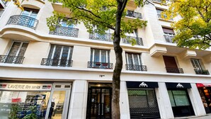 A multi-story building with balconies, a storefront with a sign reading 'LAVERIE libre service,' and a tree in the foreground. - Paris 16 Michelangelo. Les Beaux Quartiers de Paris (Paris)