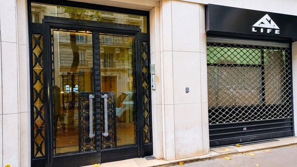 A building with a large glass entrance, a black metal gate, and a sign with 'LIFE' on it. - Paris 16 Michelangelo. Les Beaux Quartiers de Paris (Paris)