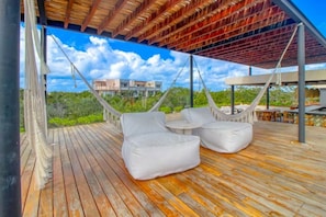 A wooden deck with a hammock and two white cushioned chairs, overlooking a building and greenery. - Stylish Tulum Studio w/ Pool & Balcony | Sleeps 4 (Tulum)