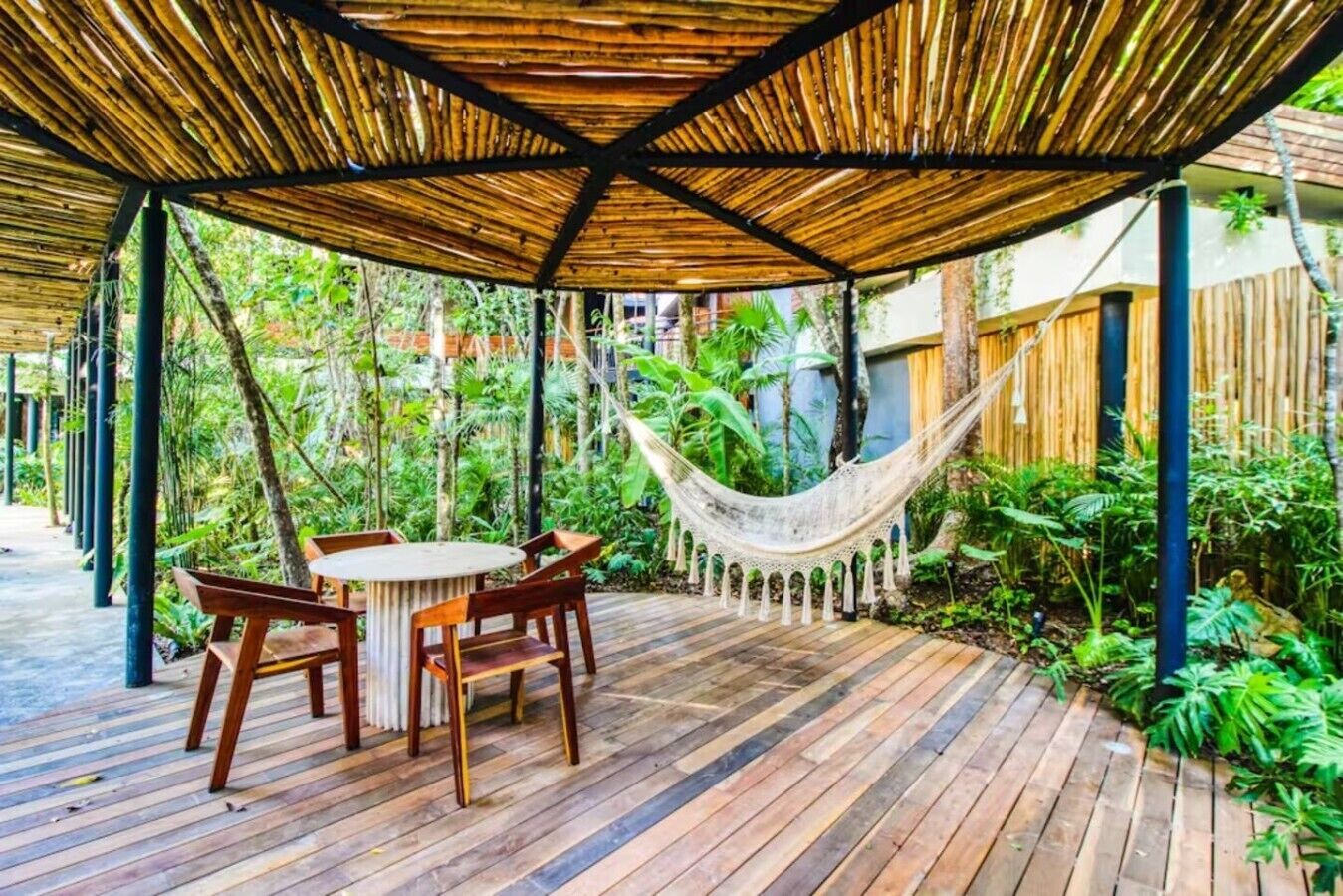 Ein überdachter Außenbereich mit Holzterrasse, einem Tisch mit Stühlen und einer Hängematte.
