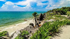 A beach with clear turquoise water, rocky shoreline, and lush greenery. - Stylish Tulum Studio w/ Pool & Balcony | Sleeps 4 (Tulum)