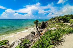 A beach with clear turquoise water, rocky shoreline, and lush greenery. - Stylish Tulum Studio w/ Pool & Balcony | Sleeps 4 (Tulum)