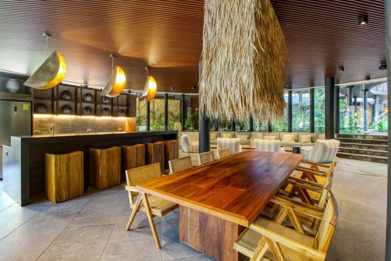 A modern interior with a wooden dining table, seating, a bar area, and a hanging light fixture.