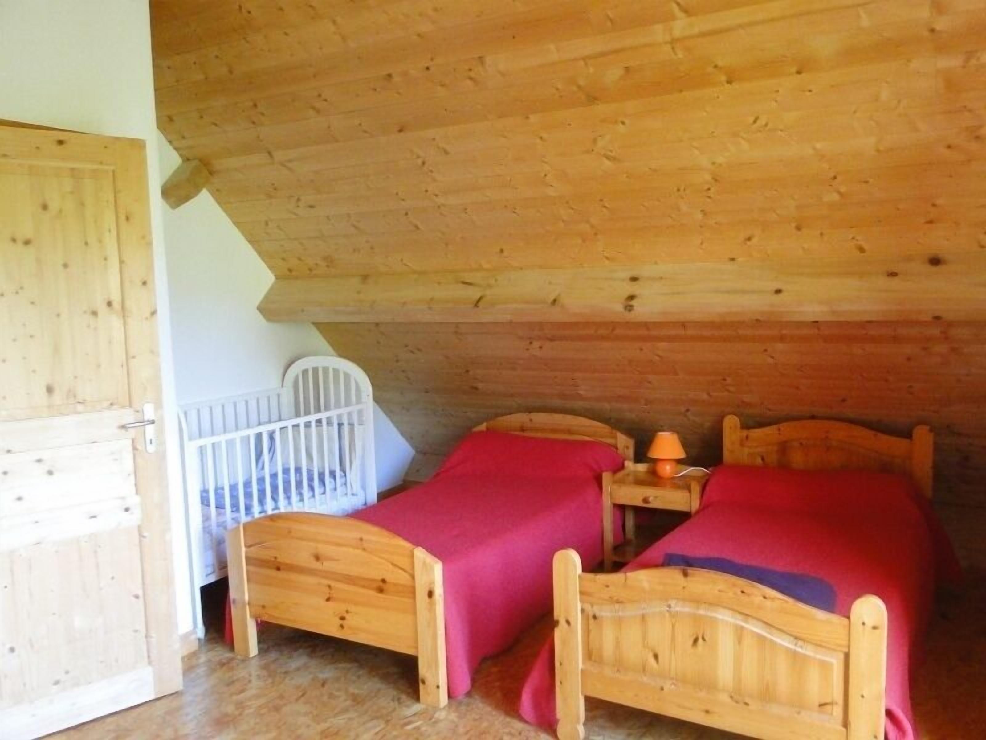 A room with two wooden beds, a white crib, and a wooden ceiling.