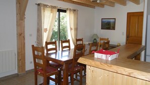 Un coin repas avec des chaises et une table en bois, une fenêtre avec des rideaux, une lampe et un tableau au mur.