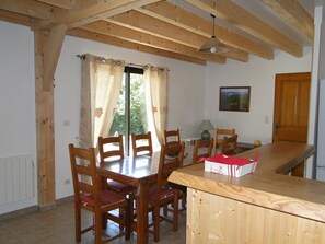 Un coin repas avec des chaises et une table en bois, une fenêtre avec des rideaux, une lampe et un tableau au mur.