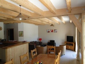 A wooden interior with a dining table, chairs, a sofa, a TV, and a kitchen area. - Le Champ de Cros - MURAT LE QUAIRE (MURAT LE QUAIRE)