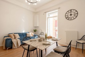 A modern living space with a dining area, a blue sofa, a table set for two, and a wall clock. - Maison Manzoni - Contemporary Elegance (Bari)