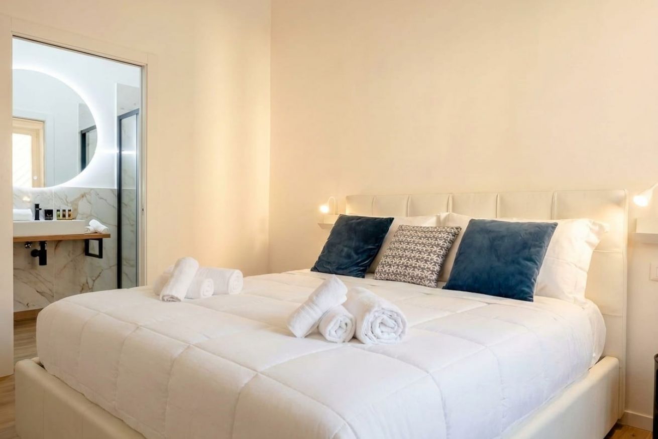 A hotel room with a bed, pillows, a mirror, and a bathroom with a marble countertop.