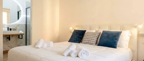 A hotel room with a bed, pillows, a mirror, and a bathroom with a marble countertop.