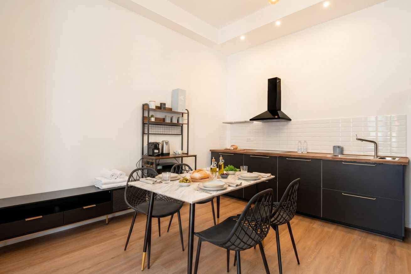 Una cocina moderna con una mesa de comedor preparada para cuatro personas, una campana extractora negra y un horno empotrado.