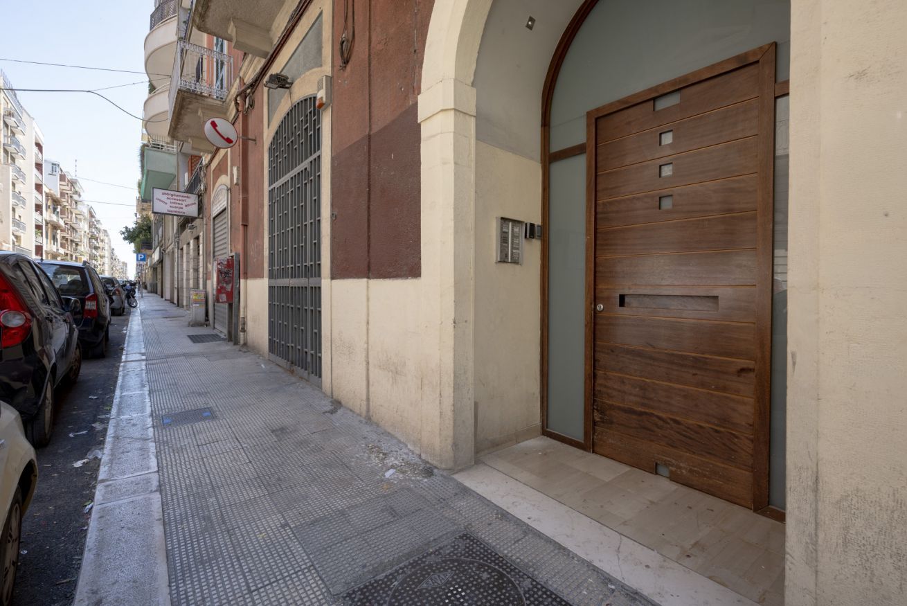 Une vue de rue avec des voitures garées, un bâtiment doté d’une grande porte en bois et un panneau avec un symbole de téléphone.