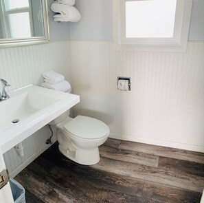A bathroom with a white sink, toilet, and wooden flooring. - Cozy 1-bedroom motel in peaceful Salida with AC (Salida)