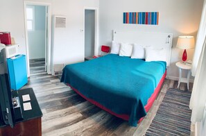 A hotel room with a bed, a desk, a microwave, a red chair, a red lamp, and a colorful artwork on the wall. - Cozy 1-bedroom motel in peaceful Salida with AC (Salida)