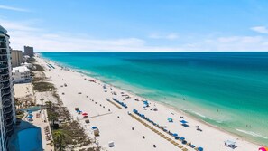 Ein Strand mit Liegestühlen und Sonnenschirmen, blauem Meer und Gebäuden entlang der Küste.
