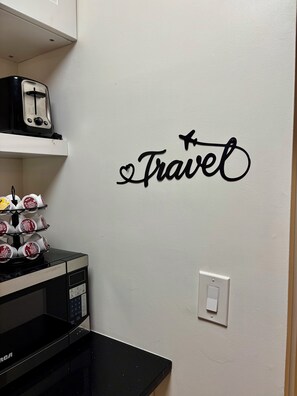 A kitchen with a toaster, a microwave, and a wall decoration that says 'Travel' with a heart and an airplane.