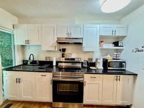 A modern kitchen with white cabinets, stainless steel appliances, and a black countertop. - Modern Abbotsford Retreat | Private Suite Near Downtown | Sleeps 4 (Abbotsford)
