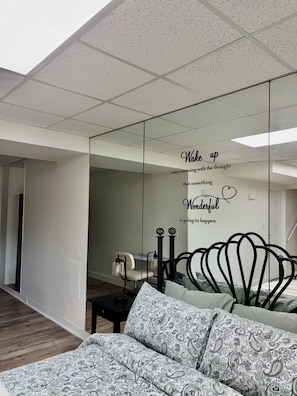 A modern bedroom with a bed, a bedside table, a mirror, and a motivational quote on the wall.
