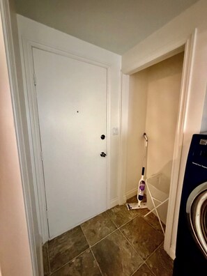 A hallway with a white door, a vacuum cleaner, and a washing machine.