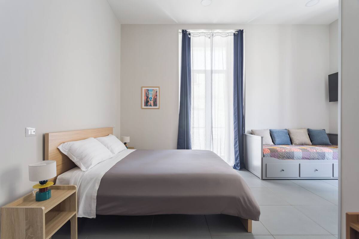 A bedroom with a bed, bedside table, lamp, and a window with curtains.