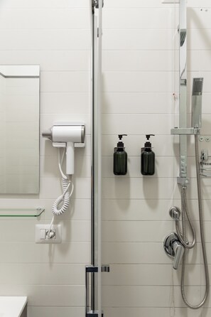 Une douche Ă©quipĂ©e dâun sĂšche-cheveux portatif, de deux bouteilles de shampoing et dâune Ă©tagĂšre en verre.