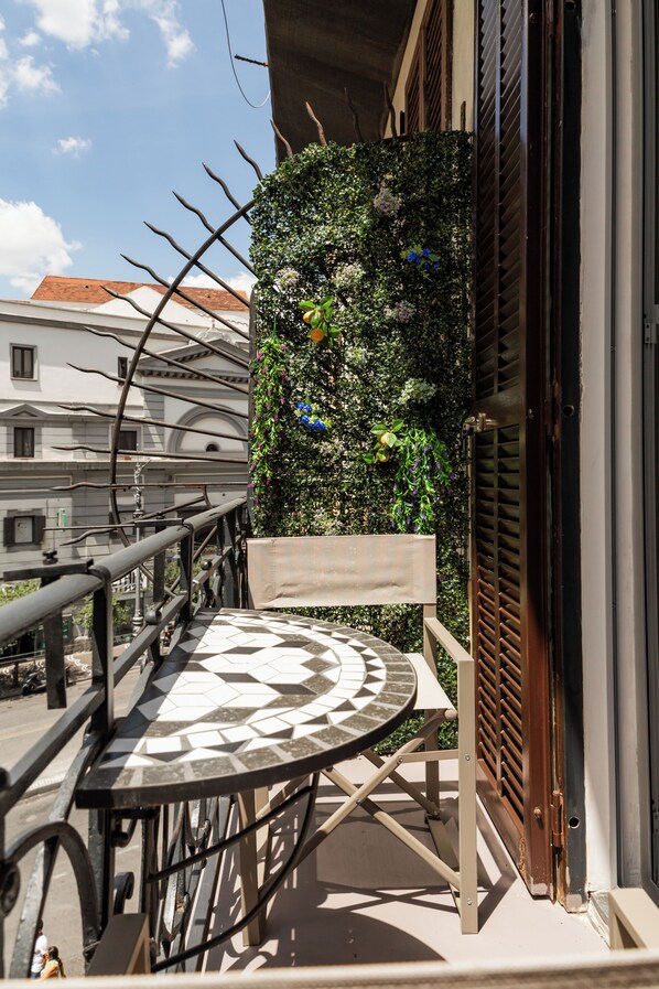 Un balcon dotĂ© dâune balustrade en mĂ©tal, une table ronde au plateau Ă motifs et un jardin vertical agrĂ©mentĂ© de diverses plantes et fleurs.
