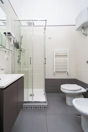 Une salle de bain moderne avec une douche à parois de verre, des toilettes blanches et un lavabo doté d’un plan de travail foncé.